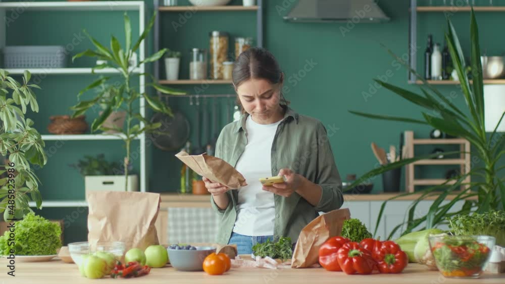 A Young Woman is Studying the Composition of Products Using a Mobile Application in the Kitchen at Home. Poor Composition, Poor Industry, Carcinogens. The Concept of Diet, Proper Nutrition and Health. A Young Woman is Studying the Composition of Products Using a Mobile Application in the Kitchen at Home. Poor Composition, Poor Industry, Carcinogens. The Concept of Diet, Proper Nutrition and Health.