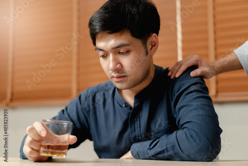 Obraz na plátně Alcoholism, depressed asian young man sitting on table while drinking alcoholic beverage, holding glass of whiskey at night