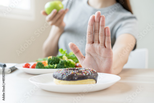 Diet, Dieting asian young woman or girl use hand push out, deny sweet donut and choose green salad vegetables, eat food for good healthy, health when hungry. Close up female weight loss person. photo