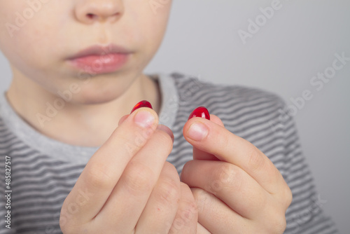 A Caucasian boy holds two red pills of a medicinal drug in his hands