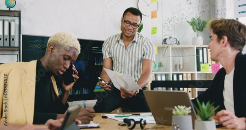 Portrait of three busy male employees, talking, working together at workplace, using electronic whiteboard, paper documents, telephone photo