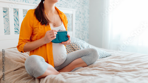 Pregnant woman holding purse in bed. Pregnant woman counting money in purse.