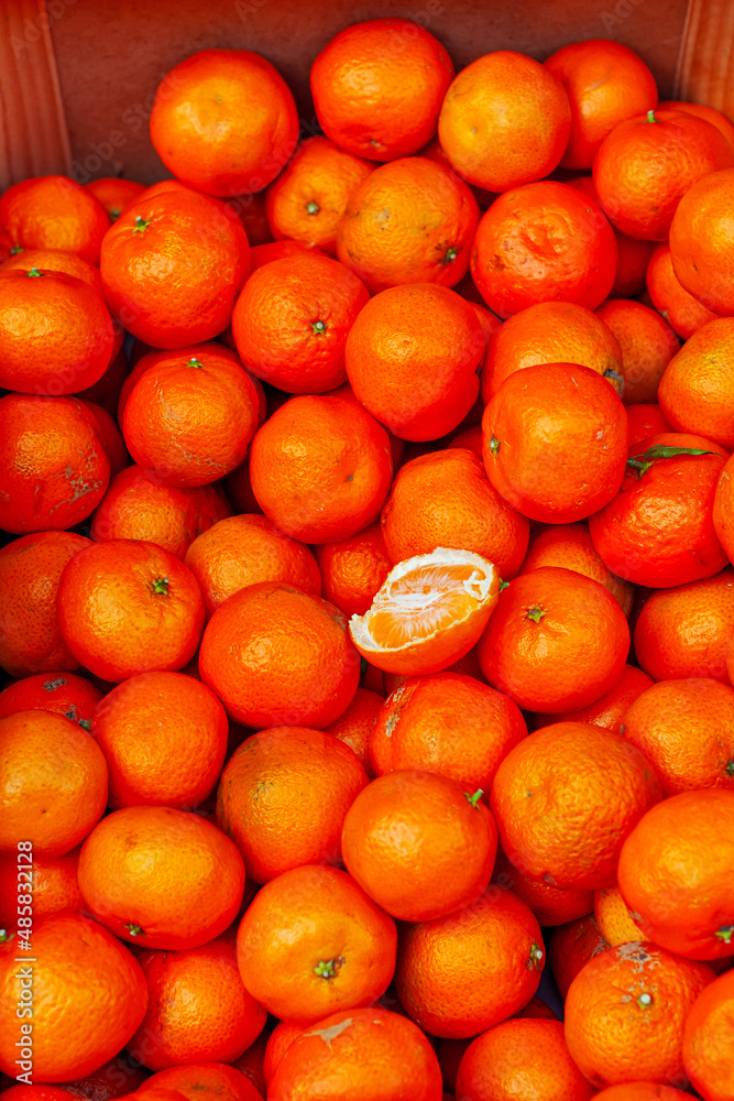 Lots of orange tangerines in a box. Texture of round tangerines close up. Sale of fruit at the market and supermarket.