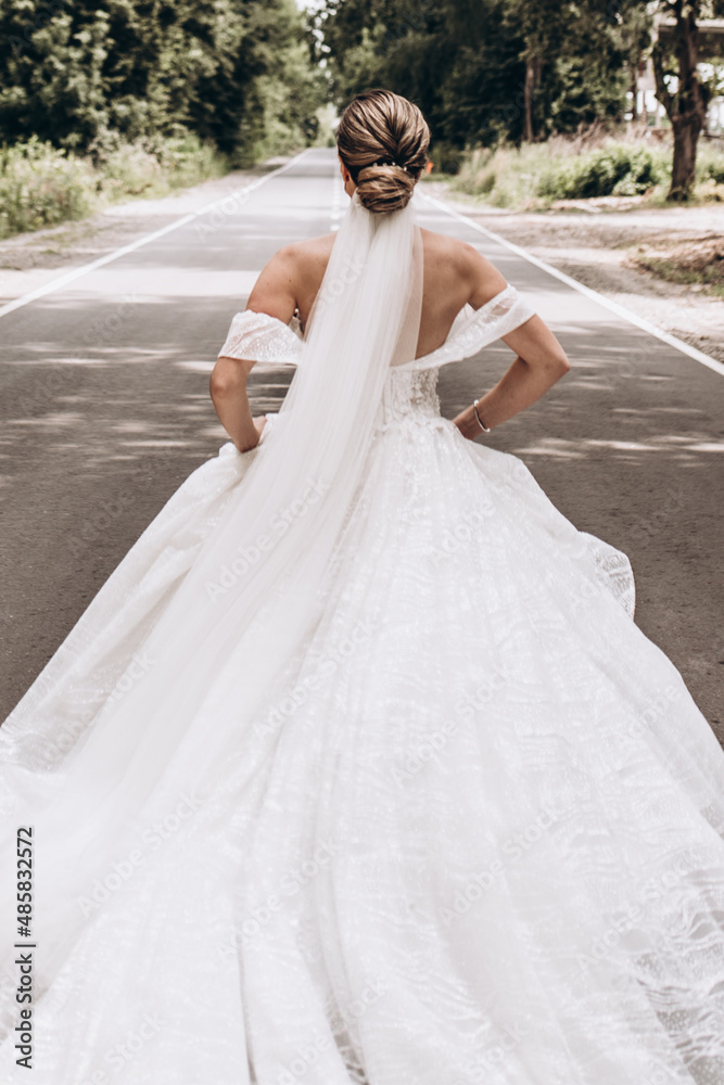 The bride in a long veil runs along the road. Photo from the back