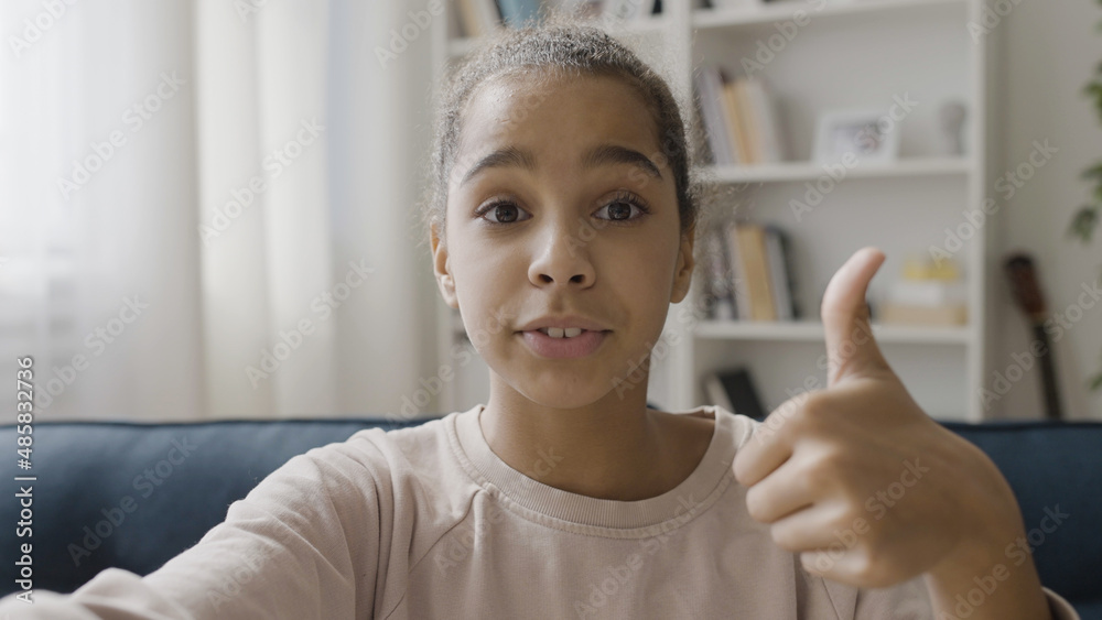 African American teenager creating content, talking to subscribers online, showing like gesture on camera