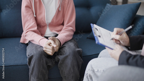 Doctor writing notes on clipboard, sitting near young patient, teen counselling
