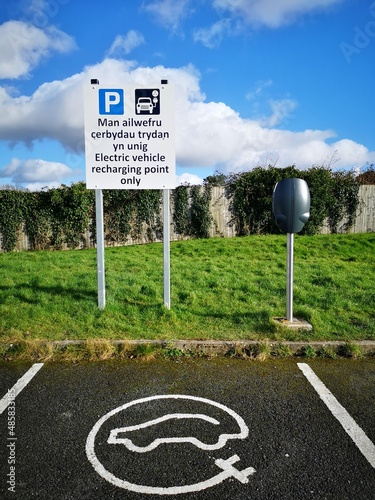 Electric vehicle recharging station in public space. Bilingual sign in English and Welsh languages - in a car park with restrictions on parking in this space to EV vehicles only.