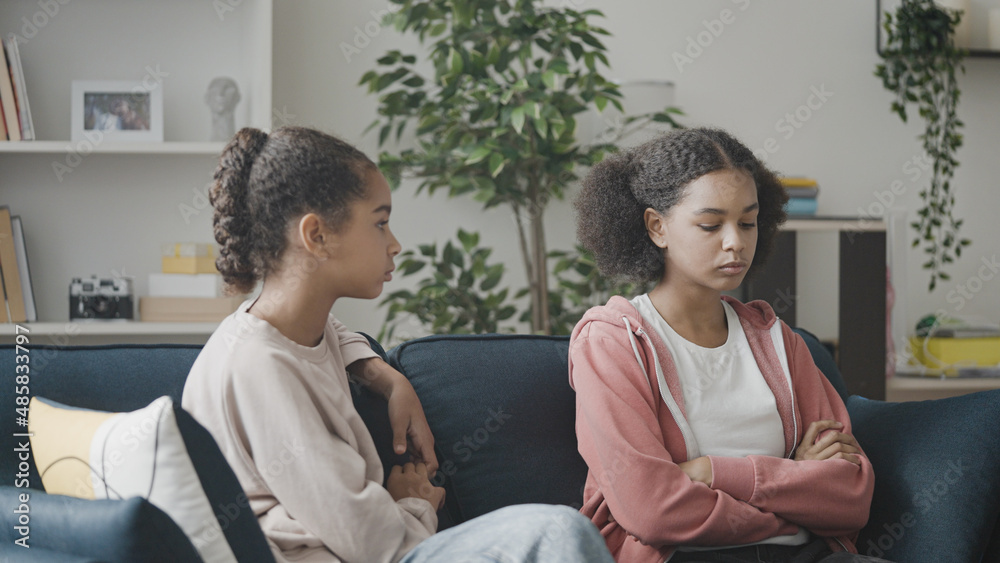 Sad teenage girls talking on couch, friends discussing problem, solving a conflict Sad teenage girls talking on couch, friends discussing problem, solving a conflict