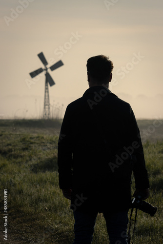 A man with a camera admires the view of a windmill with a sunrise