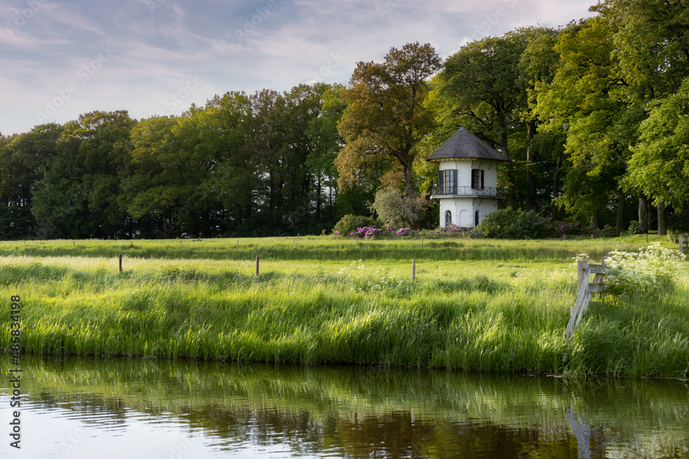 Fototapeta premium A small white tower in the middle of a meadow along a ditch in the Netherlands