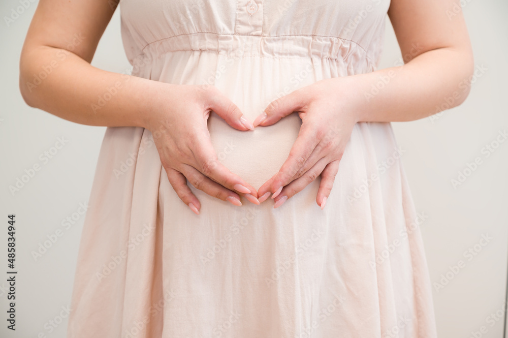 Closeup of a young pregnant woman making heart with her hands. Motherhood concept Closeup of a young pregnant woman making heart with her hands. Motherhood concept
