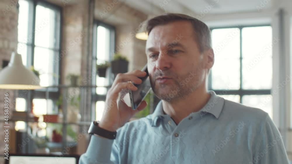 Middle aged businessman walking in office during workday and talking on mobile phone Middle aged businessman walking in office during workday and talking on mobile phone