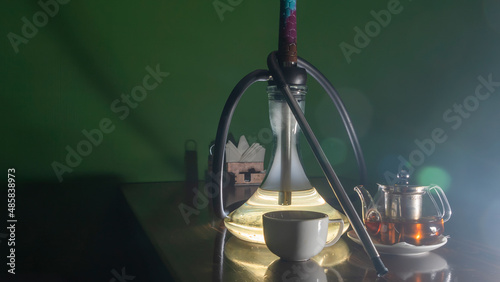 Traditional Arabian shisha and tea with lens flare. A pot of tea and Smoking hookah on a dark green background.