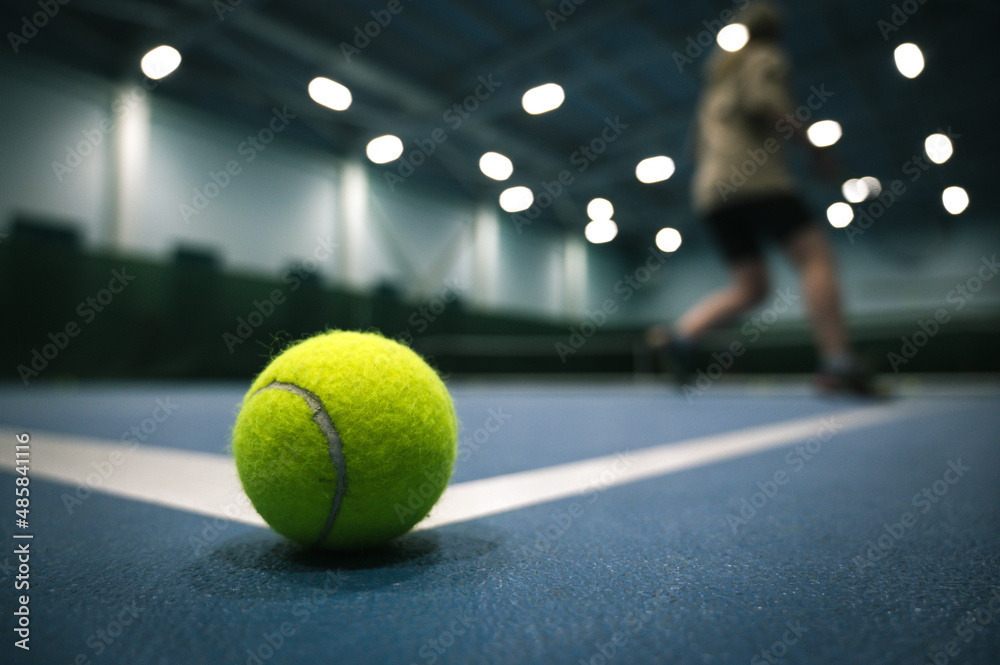 Close-up of tennis ball on blue hard court. Player in blurred background.