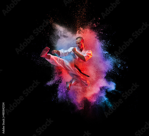 Collage. Young sportive man in white kimono practising, training martial arts, karate isolated over black background with colorful powder explosion photo