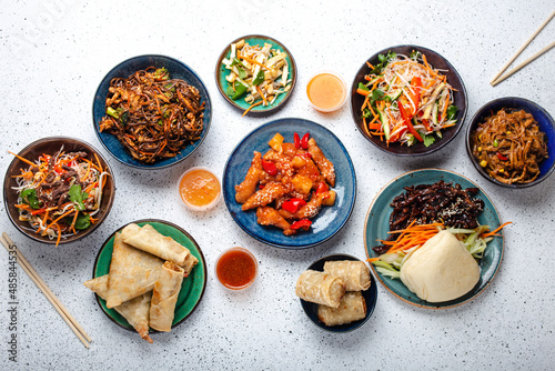 Set of Chinese dishes on white table: sweet and sour chicken, fried spring rolls, noodles, rice, steamed buns with bbq glazed pork, Asian style banquet or buffet, top view copy space 