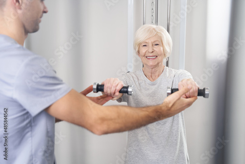 Joyful aged woman holding hand weights in front of herself