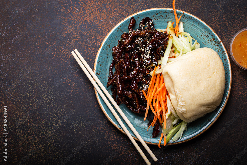 Fototapeta premium Chinese traditional dish sweet and sour deep fried glazed pork with vegetables and steamed bao bun on plate with on rustic concrete background top view, Asian meal with chopsticks
