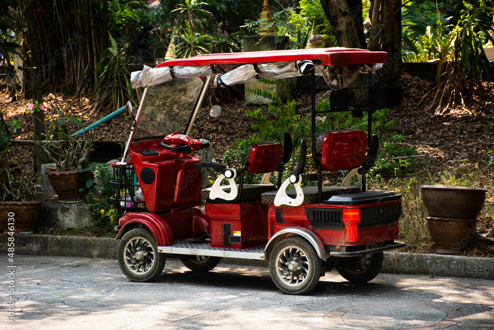 Classic modern red golf carts electric car stop on street road in garden park of Wat Samphran temple at Sam Phran city in Nakhon Pathom, Thailand