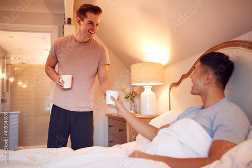 Loving Same Sex Male Couple In Bed At Home Drinking Hot Drink Together