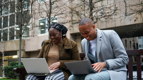 Business man and woman sitting on bench using laptops photo
