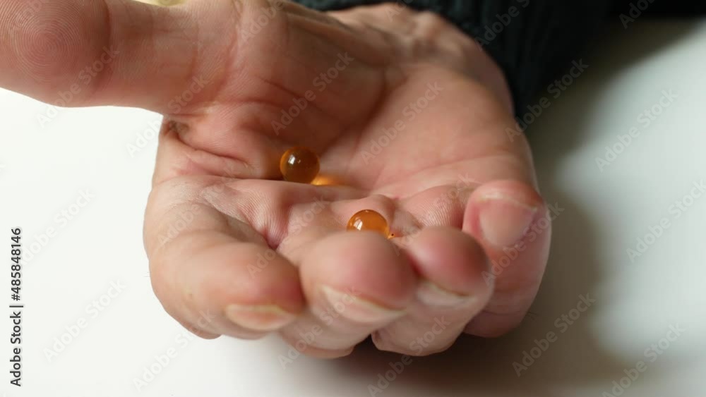 A pensioner takes vitamins omega 3 fish oil. Close-up in the hand of an elderly man transparent round capsules of a pill with omega 3 medicine. selective focus A pensioner takes vitamins omega 3 fish oil. Close-up in the hand of an elderly man transparent round capsules of a pill with omega 3 medicine. selective focus