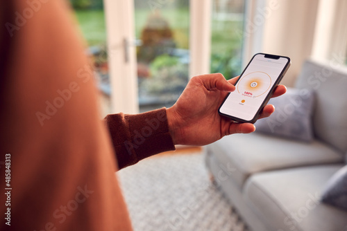 Close Up Of Man At Home Looking At App On Smart Phone To Control Lights