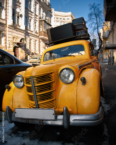 Vintage yellow car with suitcases on the roof on city street. Travel and adventure concept. Closeup. © Володимир Захаров