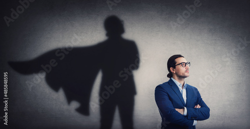 Confident businessman looking determined as casting a powerful superhero shadow on the wall. Motivated and ambitious business person shows inner strength. Hero leadership and power concept