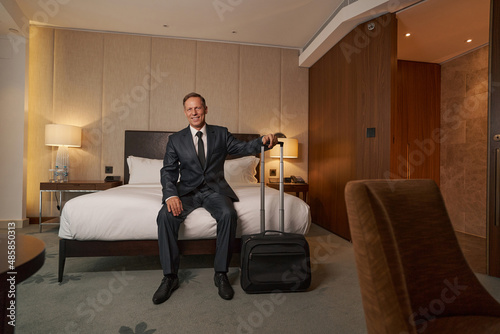 Friendly bussinesman smiling while sitting on hotel bed