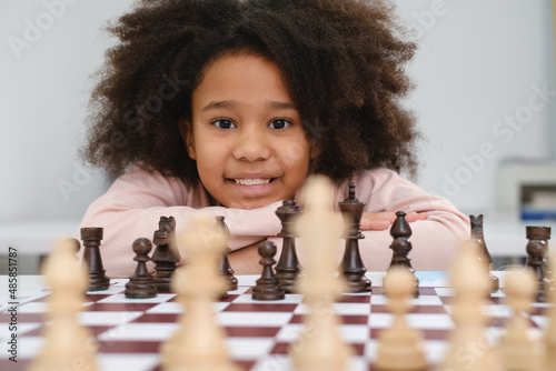 African American girl playing chess. Happy smiling child behind chess smiling in class or school lesson. Excited clever black kid with board game close-up photo