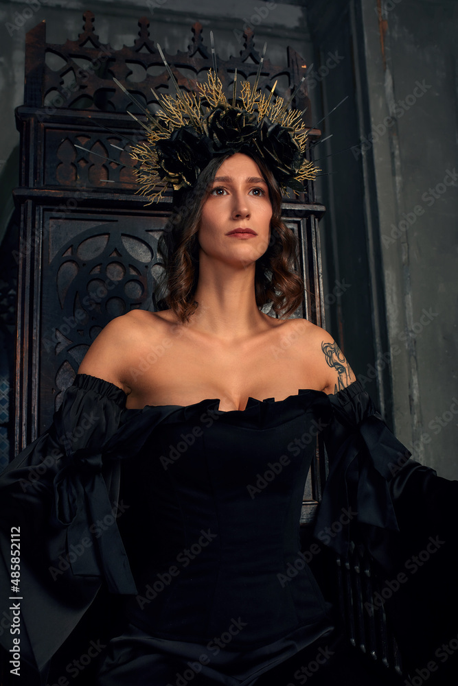 Portrait of a beautiful medieval young woman in black dress In stylish crown sitting on a throne. The Middle Ages history Portrait of a beautiful medieval young woman in black dress In stylish crown sitting on a throne. The Middle Ages history