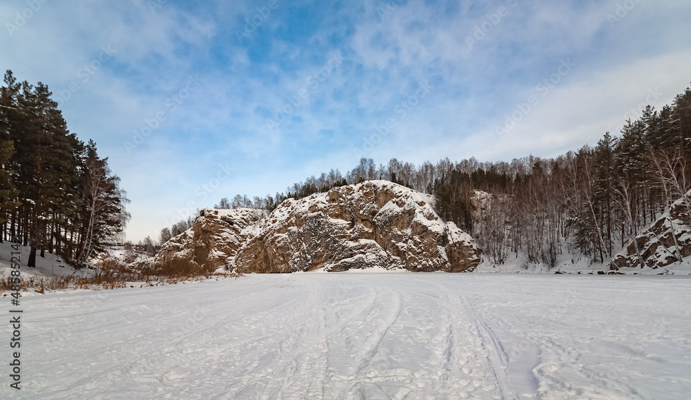 Winter landscape with a big stone, forest, sky from a frozen river