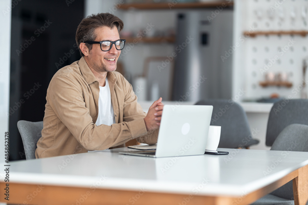 Smiling middle-aged freelancer having a video call on laptop while working remotely at home. Smiling middle-aged freelancer having a video call on laptop while working remotely at home.