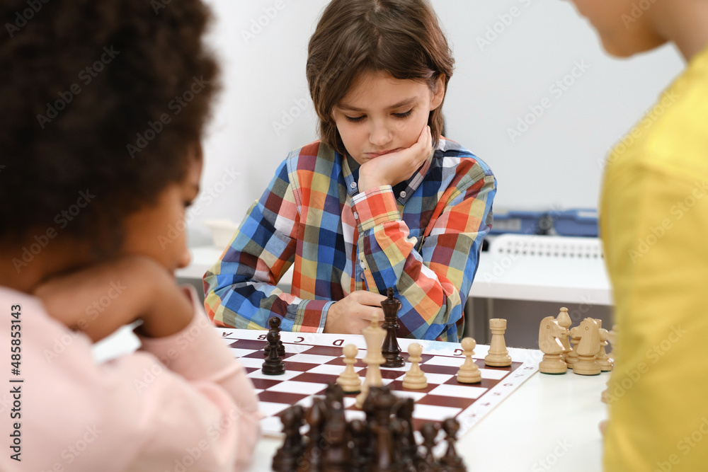 Diverse Group of kids playing chess. Concentrated multiethnic clever children with board game having fun at school. African American girl and Caucasian boys on chess lesson strategy Diverse Group of kids playing chess. Concentrated multiethnic clever children with board game having fun at school. African American girl and Caucasian boys on chess lesson strategy
