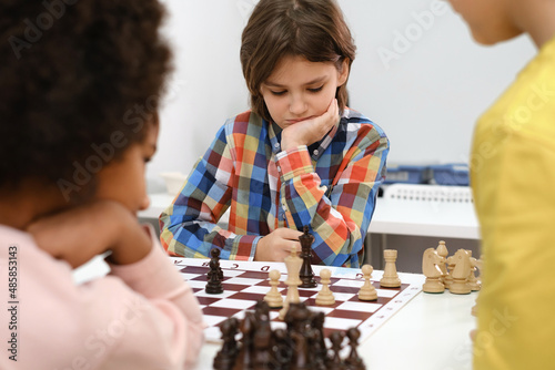 Diverse Group of kids playing chess. Concentrated multiethnic clever children with board game having fun at school. African American girl and Caucasian boys on chess lesson strategy