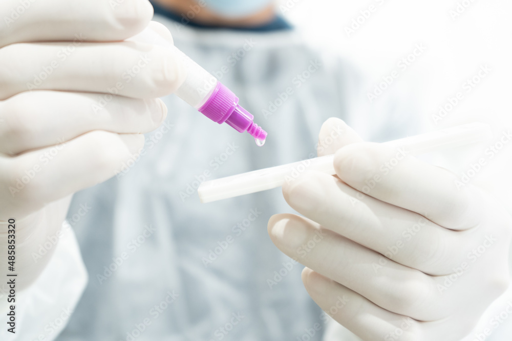 Doctor in protective suit performing an antigen test holding a tube with a drop Doctor in protective suit performing an antigen test holding a tube with a drop