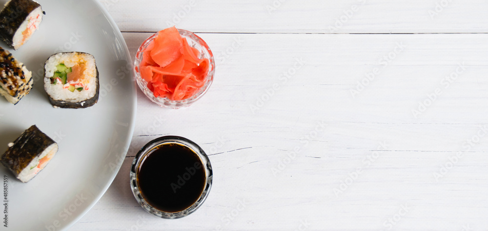 Sushi rolls on a plate on a light gray background, bamboo sticks, soy sauce and ginger, flat lay, copy space Sushi rolls on a plate on a light gray background, bamboo sticks, soy sauce and ginger, flat lay, copy space