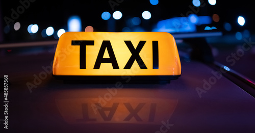 Taxi car light on dark street at night with illumination. Cab sign on the vehicle roof closeup glowing in the dusk