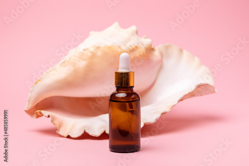 Close up of cosmetic bottle on a pink background with a decor of strombus gigas sea shell. The concept of an advertising template for beauty products photo