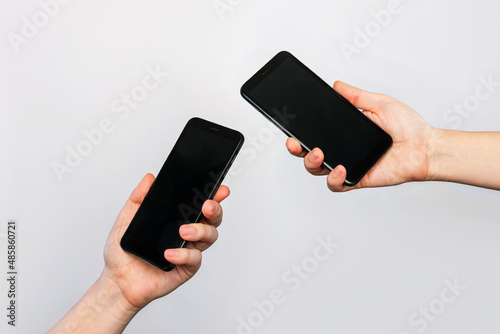 Two hands of two women holding mobile phones with blank black screens, empty copy space for design isolated on a gray background. Internet connection, File transfer via bluetooth, information exchange photo