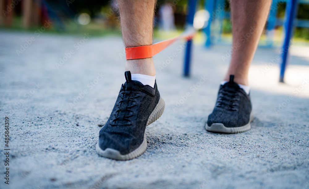 Male legs training with elastic rubber outdoors, close up