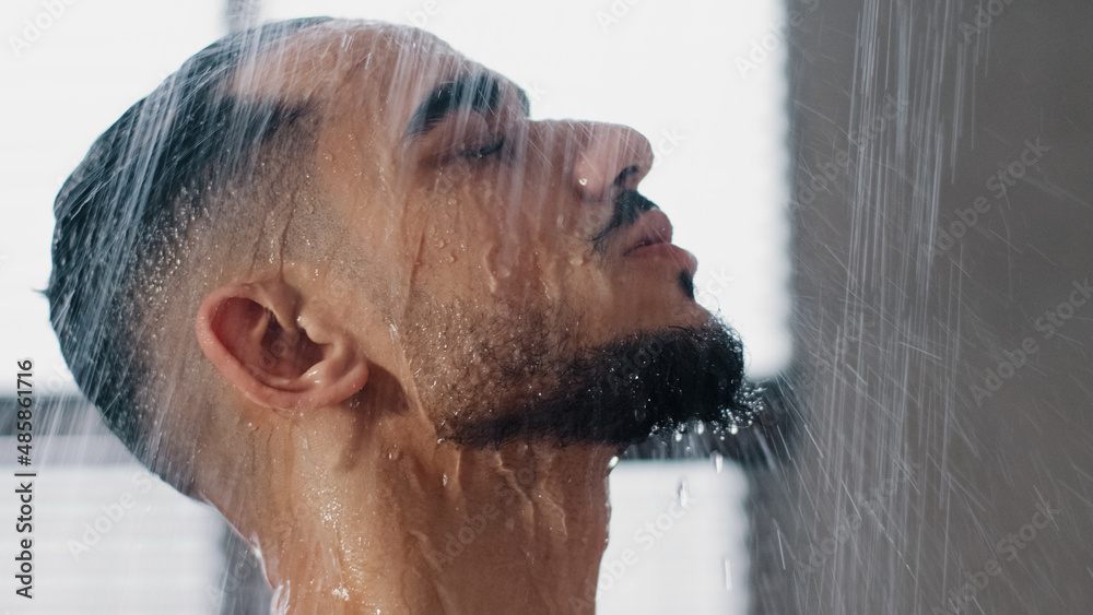 Sexy seductive arab bearded man in shower washing head showering in bathroom at home close up. Millennial brunette guy rinsing shampoo and conditioner from hair in warm bath hot water runs down face