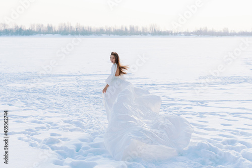 Incredible stunning girl in a white airy dress. In the background is a winter landscape of a frozen river covered in ice. Artistic photo