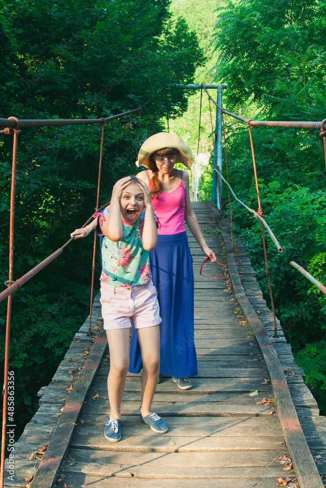 Mother and daughter going on suspension bridge summer.