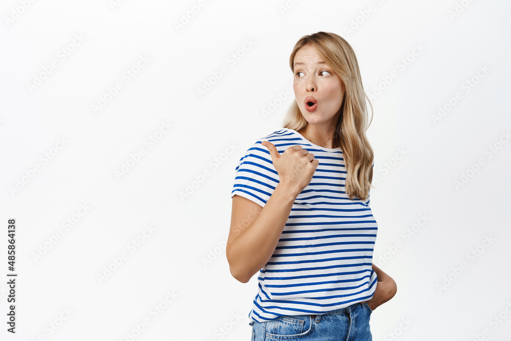 Surprised blond girl gasps and say wow, points at advertisement, shows promo banner on the left and looking fascinated at camera, checking out big sale, white background Surprised blond girl gasps and say wow, points at advertisement, shows promo banner on the left and looking fascinated at camera, checking out big sale, white background