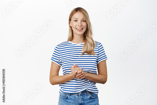 People concept. Stylish modern girl, 25 years old, standing in assistant helpful pose, ready to offer help, listening to customer and smiling, standing over white background