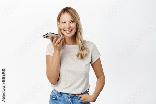 Obraz na plátne Young smiling woman using mobile phone speakerphone, translating her voice in sm