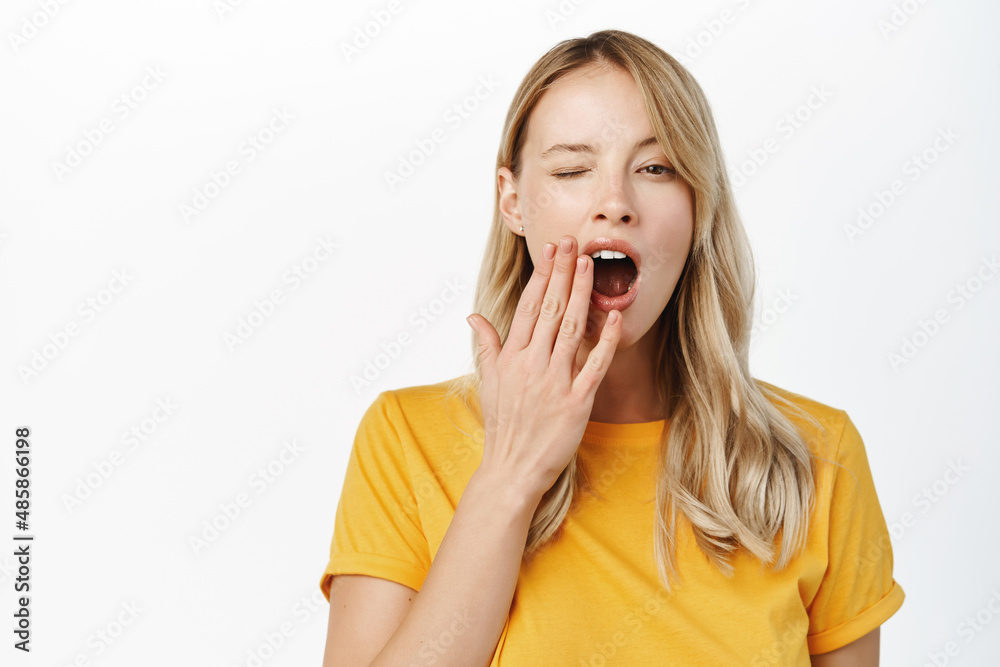 Portrait of tired girl student, young woman yawning, cover opened mouth, fatigue or boredom, standing over white background