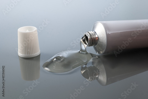 gel for external use is slightly squeezed out of the tube next to the cap on a gradient background with reflection